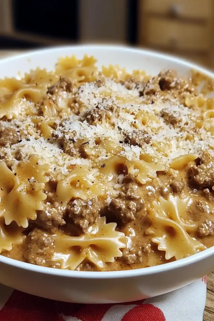 A bowl of creamy Velveeta beef pasta with bowtie noodles, topped with melted cheese and ground beef in a rich tomato cheese sauce.