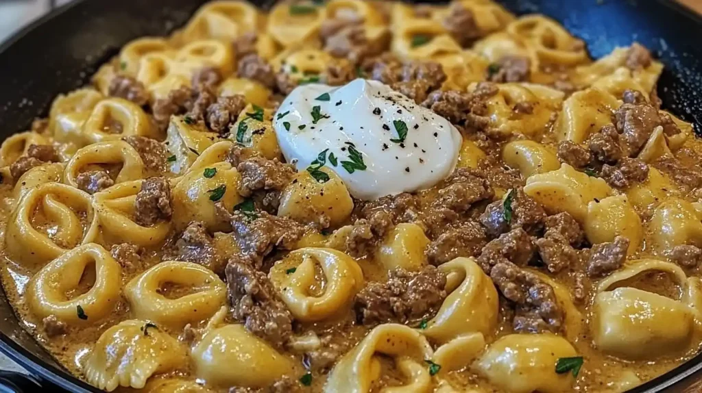 A skillet filled with creamy beef stroganoff tortellini topped with sour cream and parsley