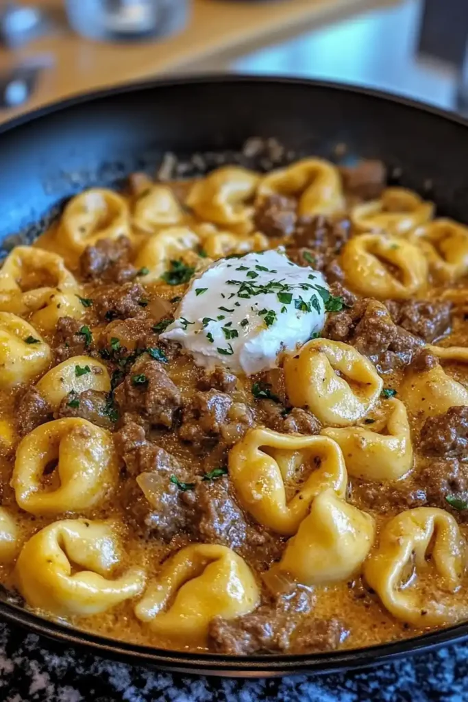 A skillet filled with creamy beef stroganoff tortellini topped with sour cream and parsley