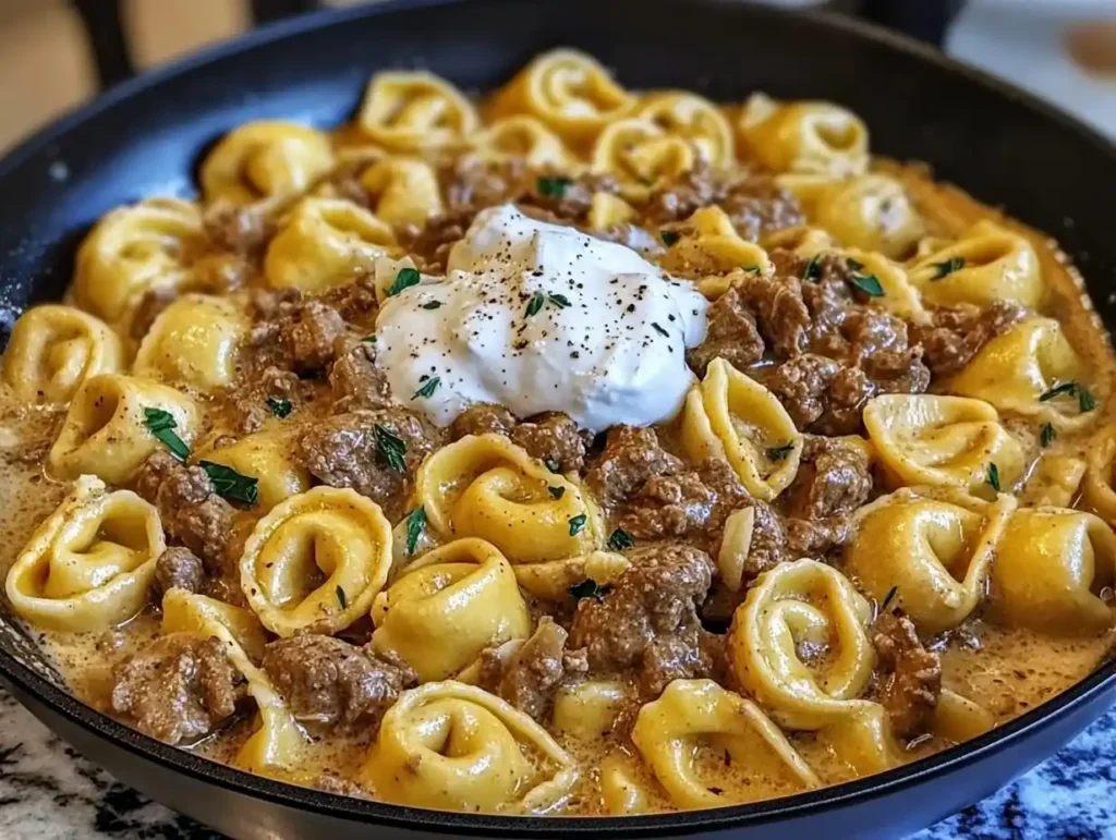 A skillet filled with creamy beef stroganoff tortellini topped with sour cream and parsley