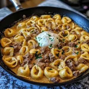 A skillet filled with creamy beef stroganoff tortellini topped with sour cream and parsley