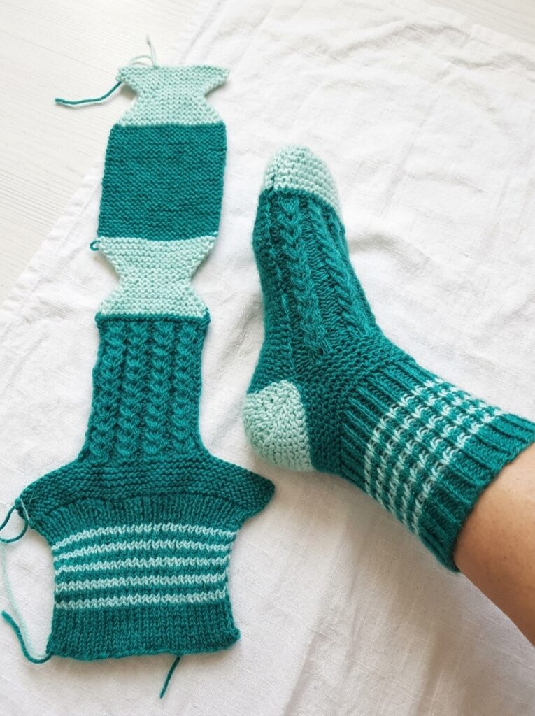 Teal and mint knitted socks with textured cable stitches, striped cuffs, and contrasting heels and toes.